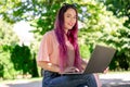 Young girl is studying in the spring park, sitting on the wooden bench and browsing on her laptop Royalty Free Stock Photo