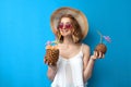 Girl in a sun hat and glasses drinks a tropical cocktail of pineapple and coconut on a blue isolated background, a woman with Royalty Free Stock Photo