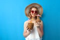 Girl in a sun hat and glasses drinks tropical cocktails made of pineapple and coconut and dreams on a blue isolated background, a Royalty Free Stock Photo