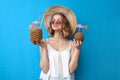 Girl in a sun hat and glasses holds tropical cocktails made of pineapple and coconut on a blue isolated background, relaxing at Royalty Free Stock Photo