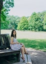 A young girl in a sundress sitting on a park bench. Beautiful woman in a summer white dress and sandals. Girl sitting on a bench