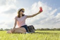 Young girl in sunglasses and hat drinks summer berry drink with ice sitting on green grass, copy space, golden hour