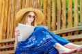 Young girl in sunglasses in a straw hat reads a glossy magazine on a bench on a background of a wooden wall. Summer mood, Royalty Free Stock Photo