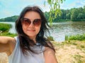 Young girl in sunglasses in white T-shirt smiling on river bank. Young smiling woman tourist standing, wearing white Royalty Free Stock Photo