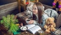 Young girl in a sweater reading a book with a mug of tea in the evening in a warm Christmas atmosphere. New year mood Royalty Free Stock Photo