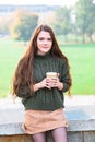 Girl enjoys smell of coffee sitting in autumn park