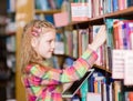 Young girl with tablet computer chooses a book in the library Royalty Free Stock Photo