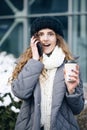 Young girl talking on her mobile phone while walking in the city street. Woman using her smartphone and holding paper Royalty Free Stock Photo