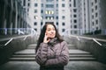 Young girl talking on mobile phone in courtyard business center. girl with long dark hair dressed in winter jacket in cold weather Royalty Free Stock Photo