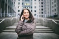 Young girl talking on mobile phone in courtyard business center. girl with long dark hair dressed in winter jacket in cold weather Royalty Free Stock Photo