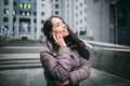 Young girl talking on mobile phone in courtyard business center. girl with long dark hair dressed in winter jacket in cold weather Royalty Free Stock Photo