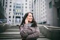 Young girl talking on mobile phone in courtyard business center. girl with long dark hair dressed in winter jacket in cold weather Royalty Free Stock Photo