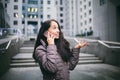 Young girl talking on mobile phone in courtyard business center. girl with long dark hair dressed in winter jacket in cold weather Royalty Free Stock Photo