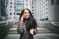 Young girl talking on mobile phone in courtyard business center. girl with long dark hair dressed in winter jacket in cold weather Royalty Free Stock Photo