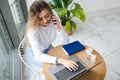 Young girl talking on mobile phone while sitting in coffee shop during and working on laptop. Royalty Free Stock Photo