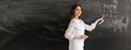 A young girl teacher or tutor is standing against the background of a chalk board with empty space for text. Math lesson