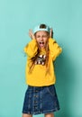 Pretty fashionable young teenager with a lovely smile posing in a baseball cap and yellow hoodie on a blue background Royalty Free Stock Photo