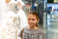 A young girl, a teenager, stands near the window of a wedding salon and looks at wedding dresses, introducing family life Royalty Free Stock Photo