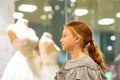 A young girl, a teenager, stands near the window of a wedding salon and looks at wedding dresses, introducing family life Royalty Free Stock Photo