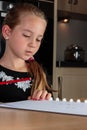 Young girl thinking while doing homework at the kitchen table holding pencil Royalty Free Stock Photo