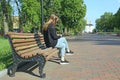 Young girl thoughtfully looking at smartphone sitting on bench in city park