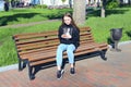 Young girl thoughtfully looking at smartphone sitting on bench in city park Royalty Free Stock Photo