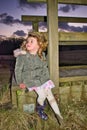 A young girl of toddler age with one wellie missing and a muddy foot, sitting on the edge of a wooden bridge.