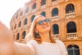 Young tourist woman in sunglasses making selfie photo on her smartphone in front of the famous Plaza de Toros de