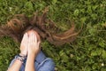 Young girl with tousled long hair lying on the green grass covering his face with his hands. Royalty Free Stock Photo