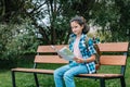 A young girl travels around the city. Cute brunette teen girl with a map is resting on a park bench. Traveling in summer vacation