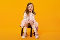 Young girl in tulle skirt and white pullover sitting on small wooden stool on bright yellow background Royalty Free Stock Photo