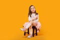 Young girl in tulle skirt and white pullover sitting on small wooden stool on bright yellow background Royalty Free Stock Photo