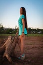 A young girl in a turquoise dress stands near a stump on the shore Royalty Free Stock Photo