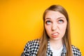 A young girl twists her mouth in disgust and looks up while standing on a yellow background