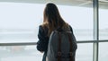 Young girl using smartphone near airport window. Happy European woman with backpack uses mobile app in terminal. 4K. Royalty Free Stock Photo