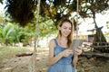 Young girl using tablet and riding swing on sand, wearing jeans sundress. Royalty Free Stock Photo