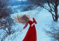 A young girl with very long hair flying in the wind. Princess in a red dress on a background of winter hills and gloomy Royalty Free Stock Photo