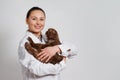 Young girl veterinarian in working clothes with a funny cat in her arms. On light background