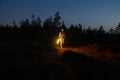 Young girl walk countryside at night hold led lamp to highlight pathway to camp or car after hiking