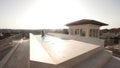 A young girl is walking along the outdoor pool on the roof of a huge house