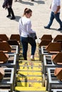 Young girl walking down stadium seats in a town with yellow stairs. Woman with white long shirt and hand bag in a village event in