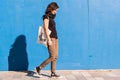 Young girl walking on street with blue wall in background.