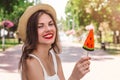 A young girl walks in the park with a lollipop in the form of watermelon. Girl in straw hat smiling in the park