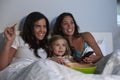 Young girl watching TV in bed with gay female parents Royalty Free Stock Photo