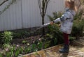 Young girl watering spring flowers with a garden hose on a sunny day.