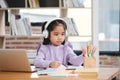 A young girl wearing headphones is sitting at a desk with a laptop Royalty Free Stock Photo