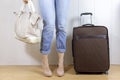 Young girl wearing jeans and high heels standing near the luggage bag and holding a handbag. Travel and relocation concept.