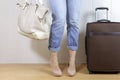 Young girl wearing jeans and high heels standing near the luggage bag and holding a handbag. Travel and relocation concept.