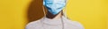 Young girl wearing medical respiratory face mask against coronavirus. Panoramic portrait on yellow background. Royalty Free Stock Photo