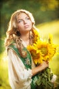 Young girl wearing Romanian traditional blouse holding sunflowers outdoor shot. Portrait of beautiful blonde girl with sunflowers Royalty Free Stock Photo